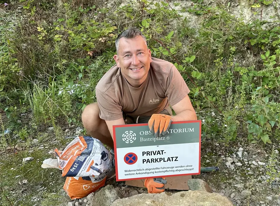 Felix, euer Gastgeber, hockt lachend mit dem Parkplatzschild des Obscuratorium am Basteiplatz