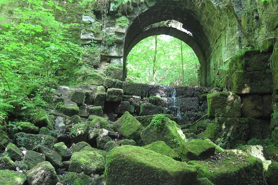 Moosbewachsene Mauerreste mit Rundbogen im Wald am Malerweg