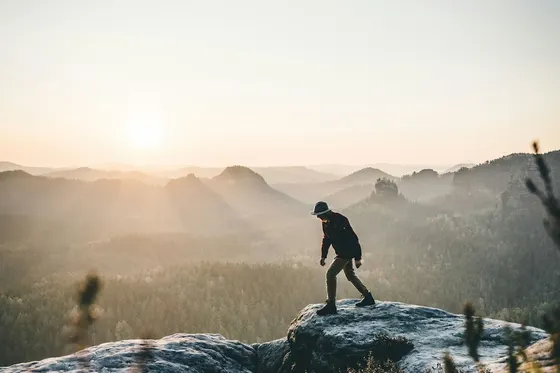 Wanderer auf einem Felsen im Abendlicht über der Landschaft