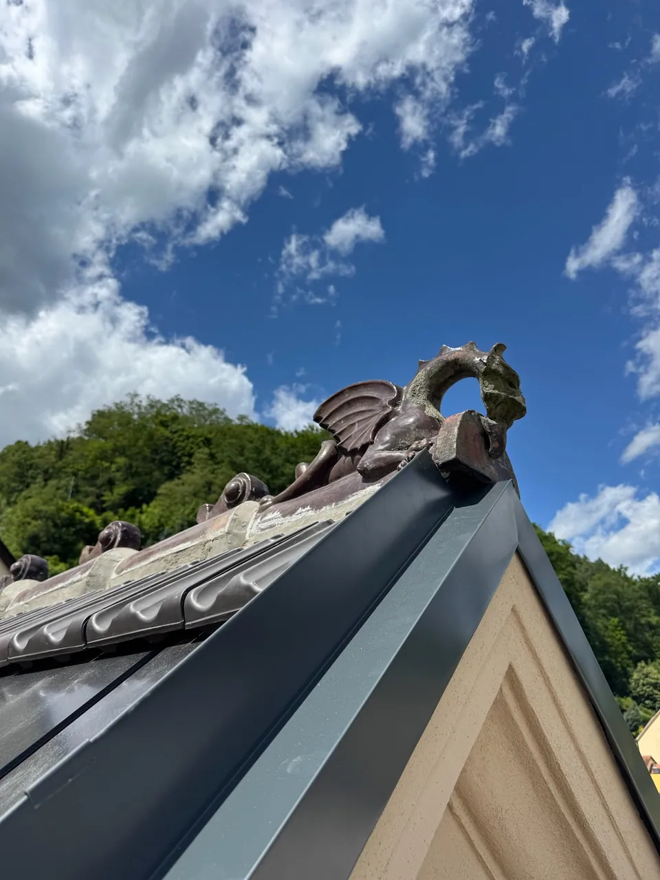 Der Keramikdrache auf dem neu gedeckten First, dahinter blauer Himmel